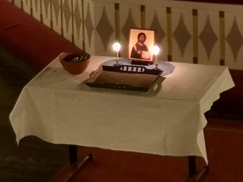 Kirkossa alttarin edessä pöytä, jossa on ikoni ja kaksi kynttilää.